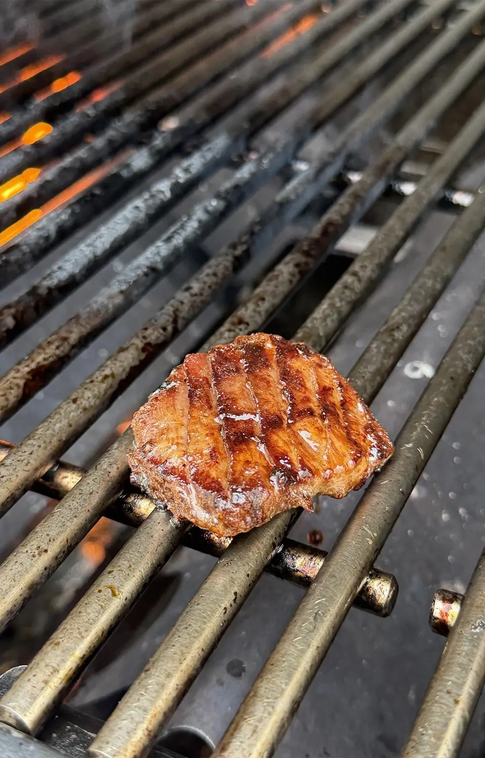 Close-up of a single thick glazed pork slice searing on a smoky barbecue grill.